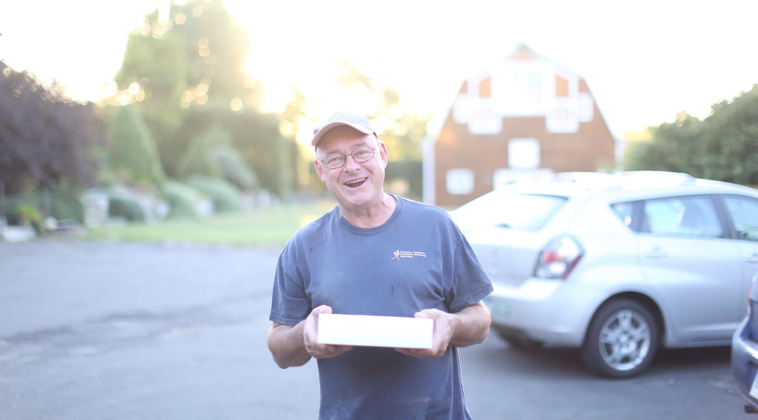 Smiling farmer holding wooden crate of prepared foods with barn in background